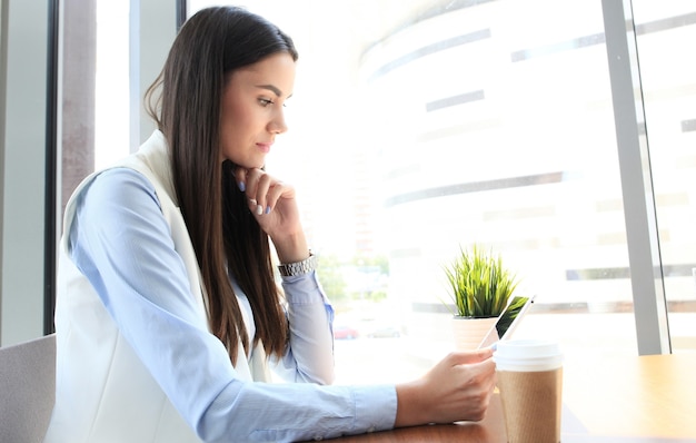 Mulher de negócios moderna tomando café no café do escritório durante a hora do almoço e usando o tablet