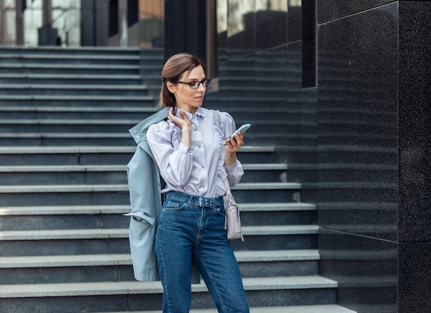 Mulher de negócios moderna usa um smartphone em pé na escada