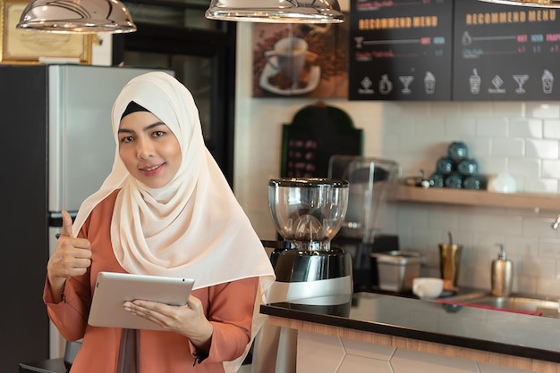 Mulher de negócios muçulmana abre a loja de café e fica em frente ao tablet de contra-ataque para receber o pedido