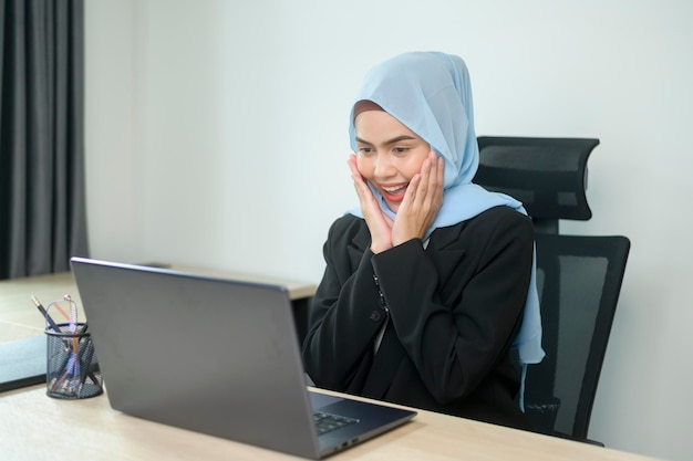 Mulher de negócios muçulmana jovem trabalhando no laptop com documentos no escritório moderno