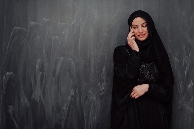 Mulher de negócios muçulmana moderna jovem usando smartphone vestindo roupas hijab na frente do quadro negro.
