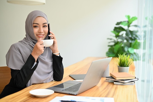 Mulher de negócios muçulmana profissional com hijab no telefonema com seu colega de trabalho tomando café