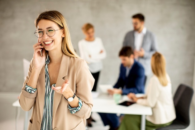 Mulher de negócios muito jovem em pé no escritório processando um celular na frente de sua equipe