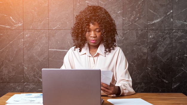 Mulher de negócios negra reunindo papéis e tipos no laptop