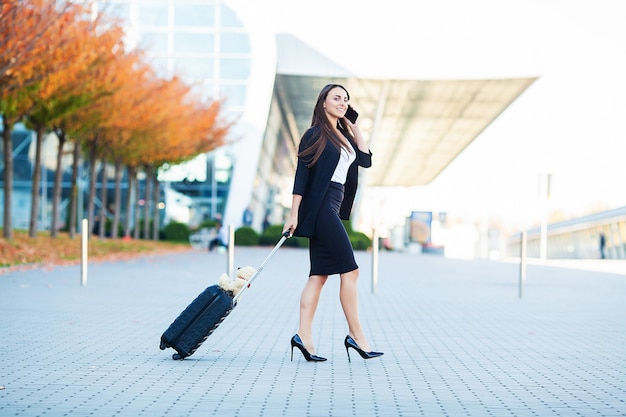 Mulher de negócios no aeroporto falando no smartphone enquanto caminhava com a bagagem de mão no aeroporto indo para o portão.