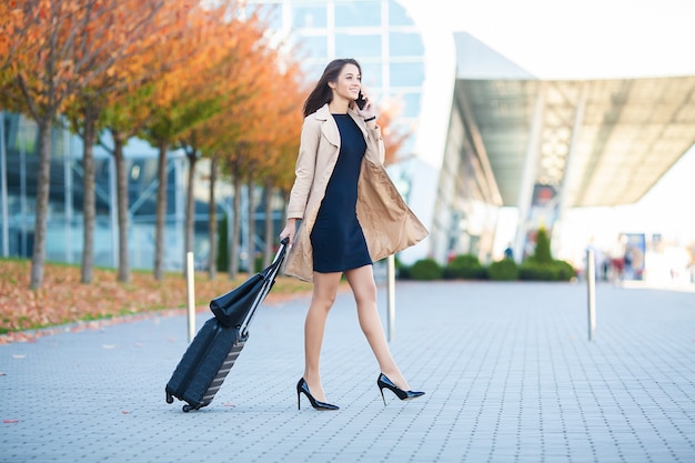 Mulher de negócios no aeroporto falando no smartphone enquanto caminhava com a bagagem de mão no aeroporto indo para o portão.