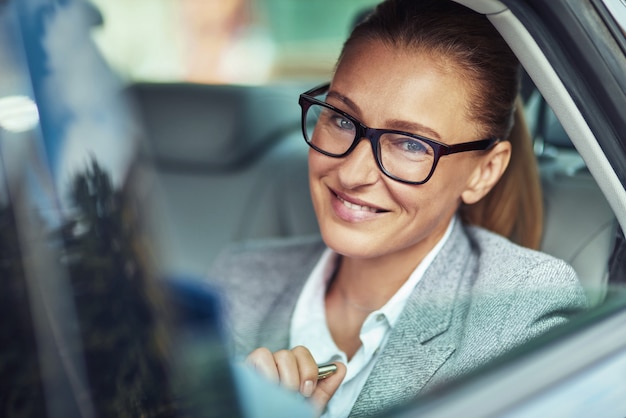 Mulher de negócios no carro. senhora alegre de meia-idade usando óculos, sentada no banco de trás do táxi, olhando para a câmera e sorrindo, conceito de transporte e veículo, executivos de táxi