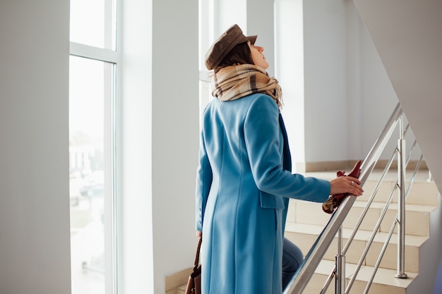 Mulher de negócios no casaco sobe as escadas no shopping. Compras. moda