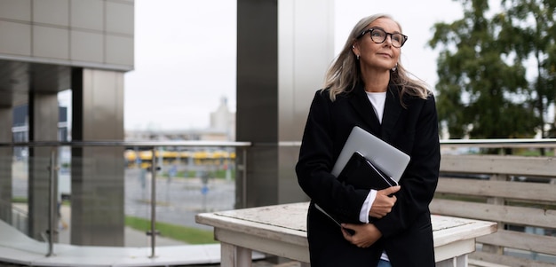 Mulher de negócios no terraço de um prédio de escritórios com um laptop nas mãos caucasiana de meia-idade