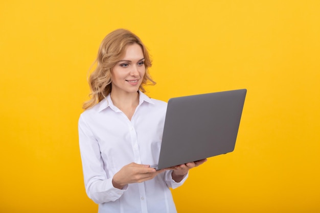 Mulher de negócios ocupada em camisa branca trabalha on-line com laptop em empresário de fundo amarelo