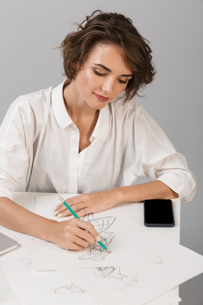 Mulher de negócios posando isolada sobre uma parede cinza, sentada à mesa usando um laptop