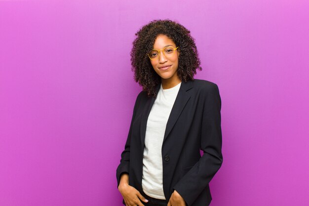 Mulher de negócios preto jovem sorrindo alegremente e casualmente com uma expressão positiva, feliz, confiante e relaxada