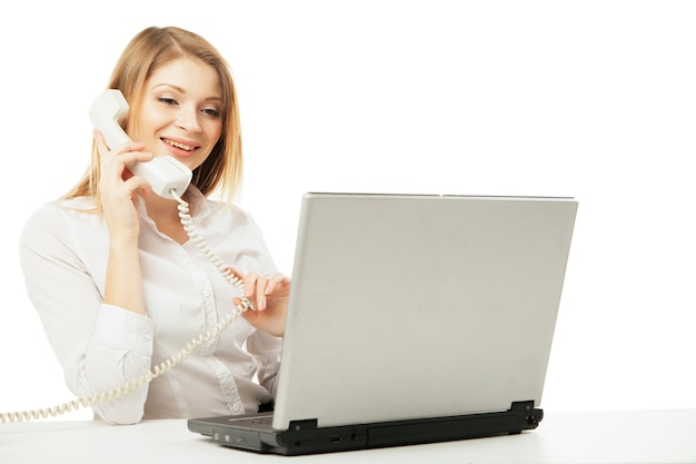 Mulher de negócios profissional jovem trabalhando em sua mesa com o laptop e sorrindo ao ligar e ter uma conversa telefônica sobre fundo branco.