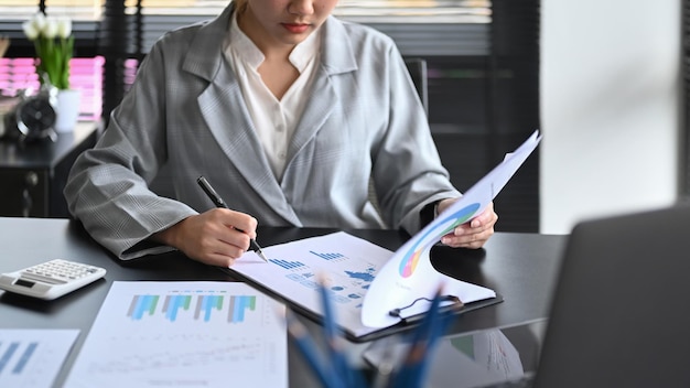 Mulher de negócios profissional usando sentado na frente do computador portátil e trabalhando com relatório financeiro na mesa de escritório