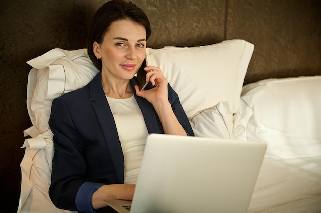 Mulher de negócios próspera bonita fazendo uma ligação ao telefone e trabalhando no laptop