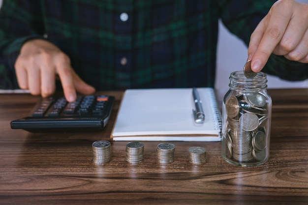 Mulher de negócios que guarda as moedas que põem no vidro e que analisam contas financeiras na mesa.