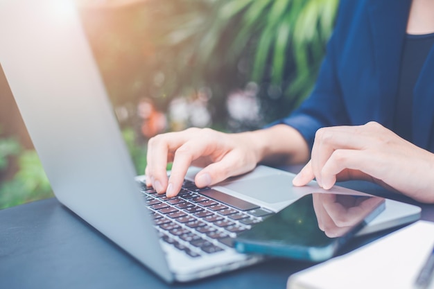 Mulher de negócios que trabalha com um computador portátil e usa um telefone celular no escritório.