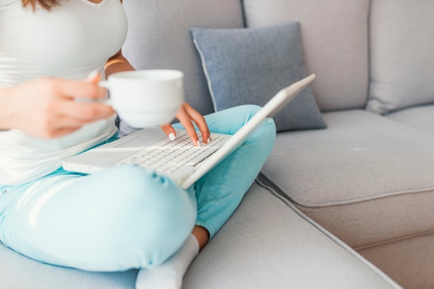 Mulher de negócios que trabalha no computador portátil que senta em casa guardando um copo de café à disposição. Wom