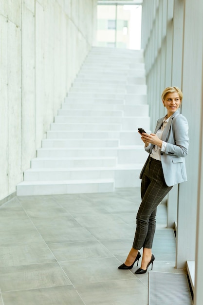 Mulher de negócios que usa o telefone celular no corredor moderno do escritório