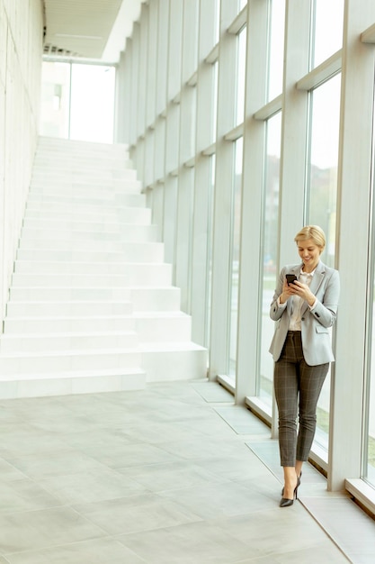 Mulher de negócios que usa o telefone celular no corredor moderno do escritório