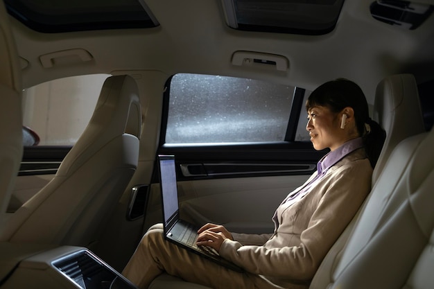 Foto mulher de negócios rica trabalhando em computador portátil enquanto viaja em um carro de luxo