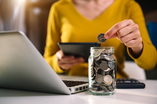 Mulher de negócios segurando moedas colocando em vidro usando smartphone e calculadora para calcular o conceito de economia de dinheiro para contabilidade financeira