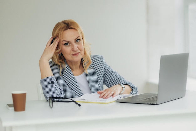 Mulher de negócios sênior cansada está usando laptop para trabalhar em ambientes fechados Uma bela senhora mais velha tem dor de cabeça por excesso de trabalho Mulher madura 50 anos