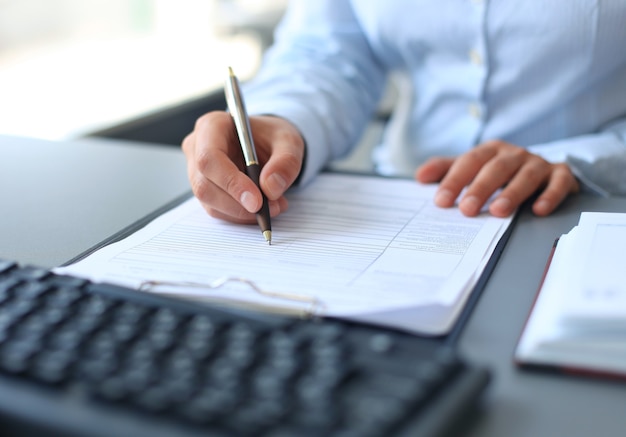 Mulher de negócios sentada na mesa do escritório, assinando um contrato com foco superficial na assinatura.