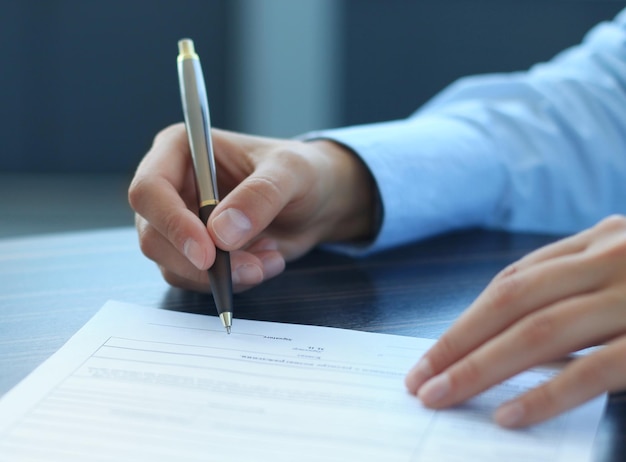 Foto mulher de negócios sentada na mesa do escritório, assinando um contrato com foco superficial na assinatura.