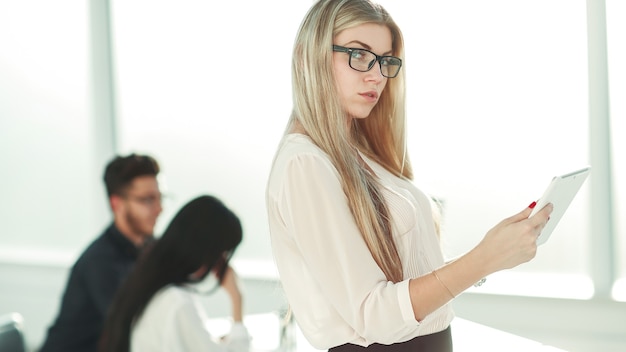 Mulher de negócios séria com tablet digital em pé perto da mesa do escritório