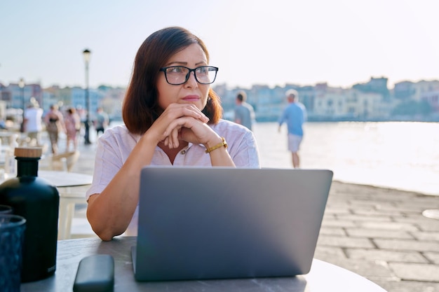 Mulher de negócios séria de meia-idade no café ao ar livre usando laptop