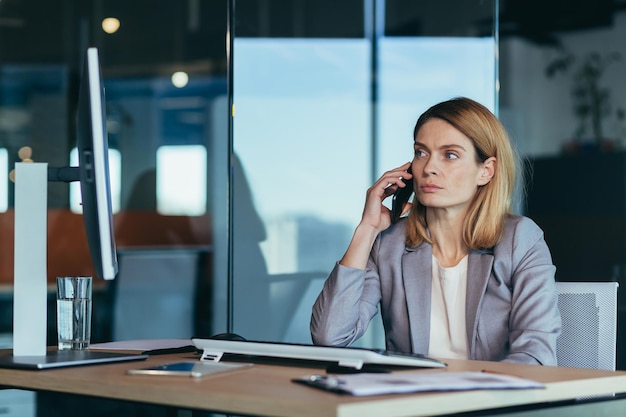 Mulher de negócios séria e ansiosa falando ao telefone trabalhando em um escritório moderno no computador foto aproximada de uma conversa de negócios