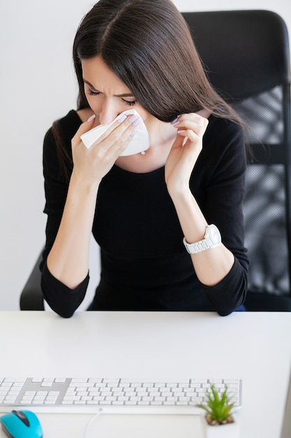 Mulher de negócios, sofrendo no trabalho atrás da mesa em seu escritório e tendo problemas de alergia