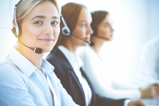 Mulher de negócios sorridente alegre com fones de ouvido, consultoria de clientes. grupo de diversos operadores de telefone no trabalho no escritório ensolarado. conceito de centro de atendimento e pessoas de negócios.