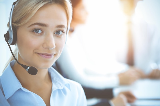 Mulher de negócios sorridente alegre com fones de ouvido, consultoria de clientes. Grupo de diversos operadores de telefone no trabalho no escritório ensolarado. Conceito de centro de atendimento e pessoas de negócios.