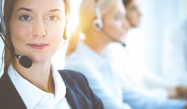 Mulher de negócios sorridente alegre com fones de ouvido, consultoria de clientes. Grupo de diversos operadores de telefone no trabalho no escritório ensolarado. Conceito de centro de atendimento e pessoas de negócios.