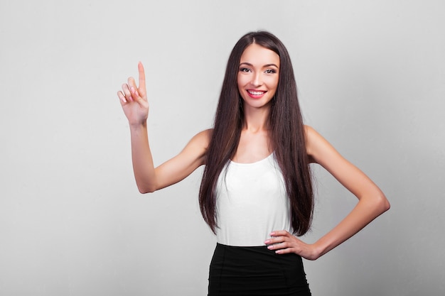 Mulher de negócios sorridente apontando para cima e olhando para a frente sobre a parede cinza