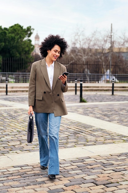 Mulher de negócios sorridente caminha usando um telefone inteligente