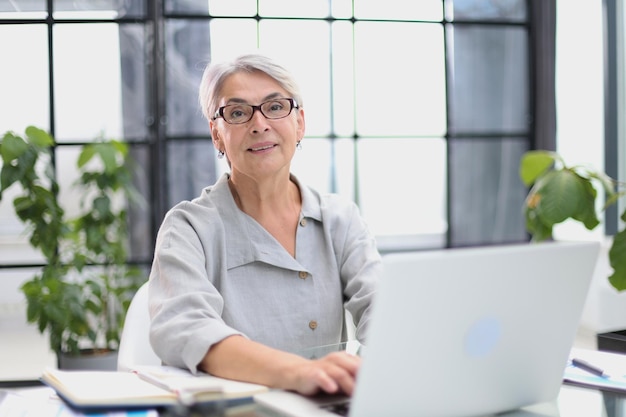 Mulher de negócios sorridente de 60 anos usando um computador