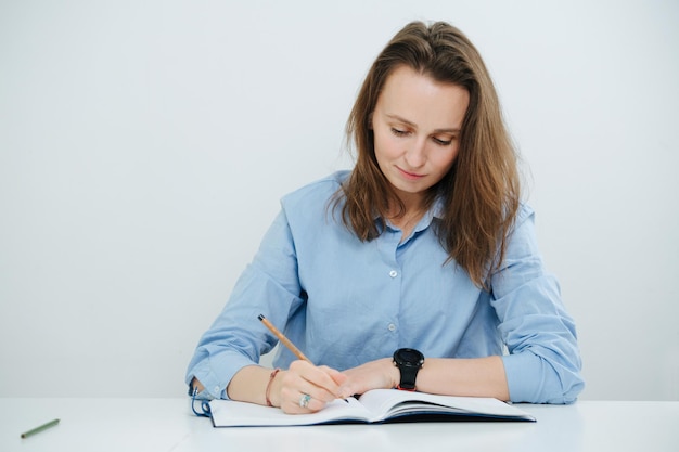 Mulher de negócios sorridente diligente em camisa azul, escrevendo em um diário