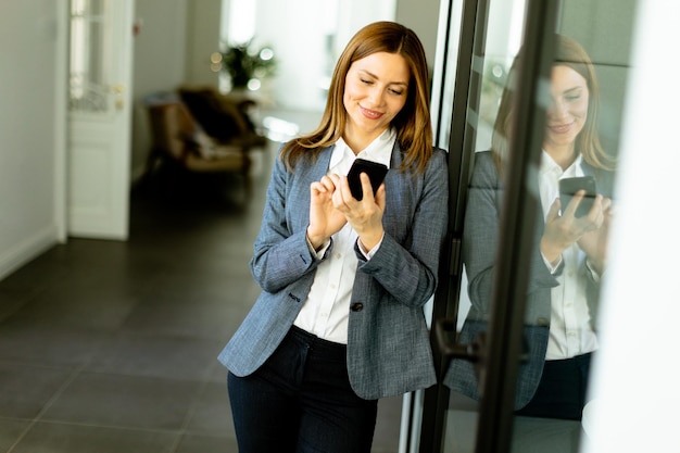 Foto mulher de negócios sorridente em um escritório moderno segurando um smartphone desfrutando de um dia de trabalho bem sucedido