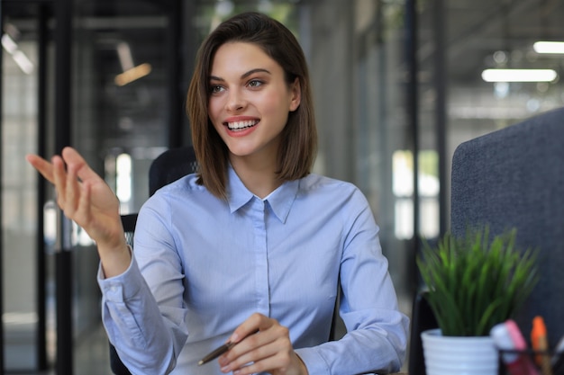 Mulher de negócios sorridente, olhando para a câmera, fazer uma conferência ou chamada de negócios, gravando um videoblog, conversando com o cliente.