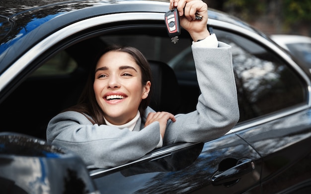 Mulher de negócios sorridente, olhando pela janela e mostrando as chaves do carro