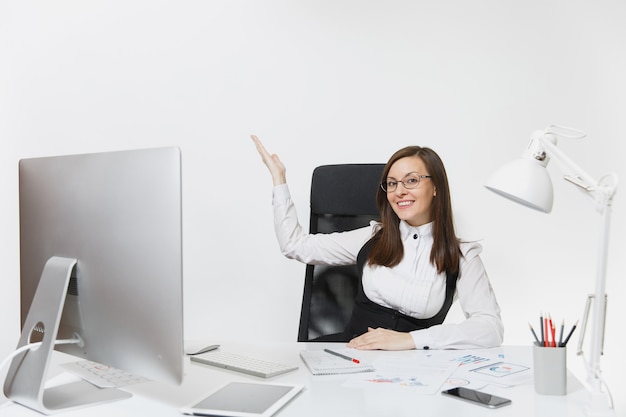 Mulher de negócios sorridente, sentada à mesa, trabalhando no computador com documentos em um escritório leve