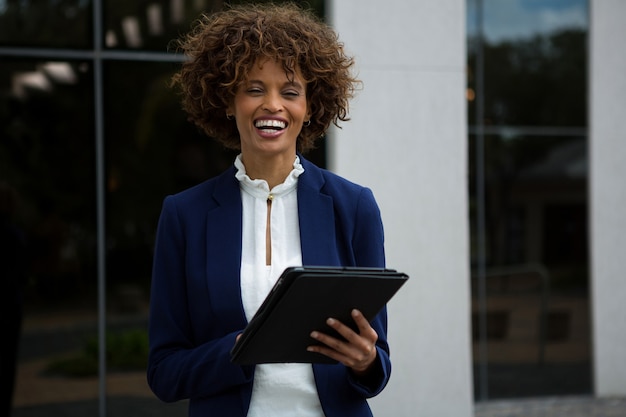 Mulher de negócios sorridente usando tablet digital perto de prédio de escritórios