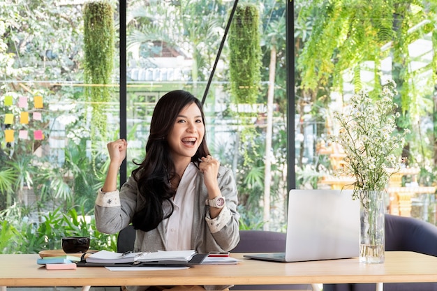 Foto mulher de negócios, sorrindo com os braços para cima comemorando para o trabalho de sucesso no escritório