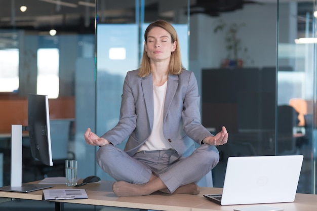 Mulher de negócios sozinha sentada à mesa em seu escritório funcionária meditando em posição de lótus