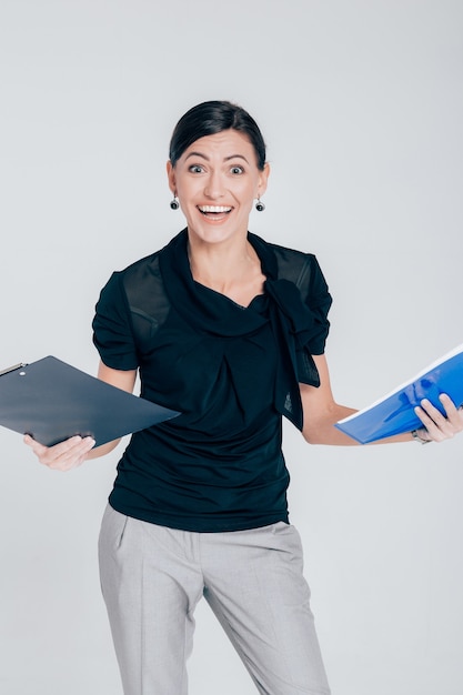 Mulher de negócios surpresa sorridente segurando uma pasta com documentos em um fundo cinza