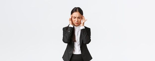 Mulher de negócios tentando se concentrar sofrendo enxaqueca antes de importante reunião de negócios empresária asiática tocando templos e fazendo caretas de dor com dor de cabeça fundo branco