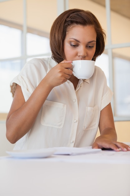 Mulher de negócios tomando café enquanto trabalha no plano no escritório